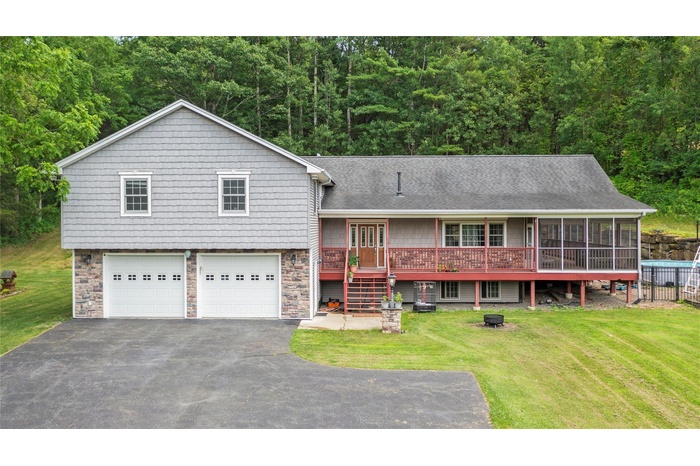 View of front of house featuring an attached garage, driveway, stone siding, and a front lawn