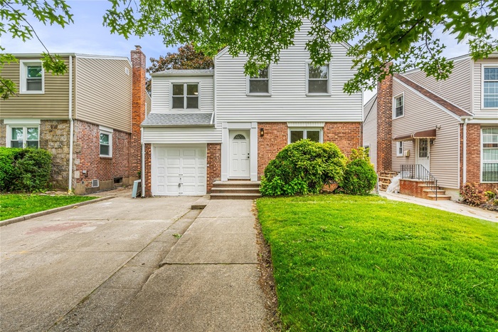 View of front of property featuring driveway, a front lawn, brick siding, and an attached garage