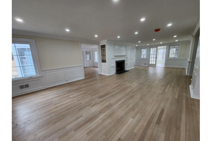 Unfurnished living room with a decorative wall, wainscoting, ornamental molding, light wood-style flooring, and a fireplace