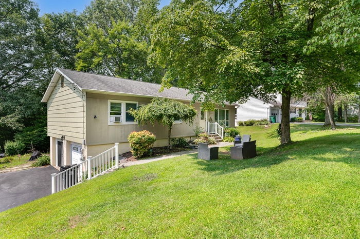 View of front of property with an attached garage, driveway, a shingled roof, and a front yard