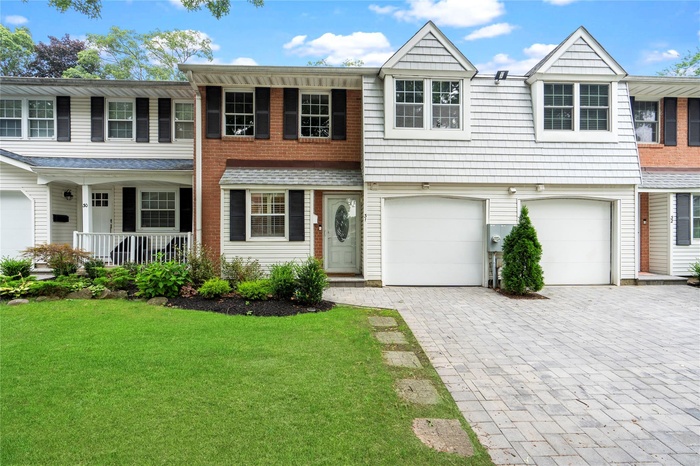View of front of property with covered porch, decorative driveway, a garage, and a front lawn
