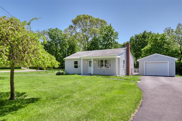 View of front of home featuring a garage, an outbuilding, a chimney, driveway, and a front lawn