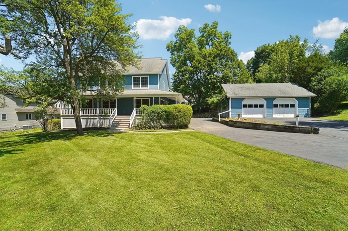 View of front of property featuring a garage, an outbuilding, covered porch, a front lawn, and roof with shingles