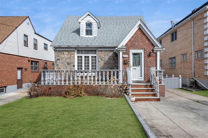 View of front facade with a porch, central AC, stone siding, roof with shingles, and a front yard