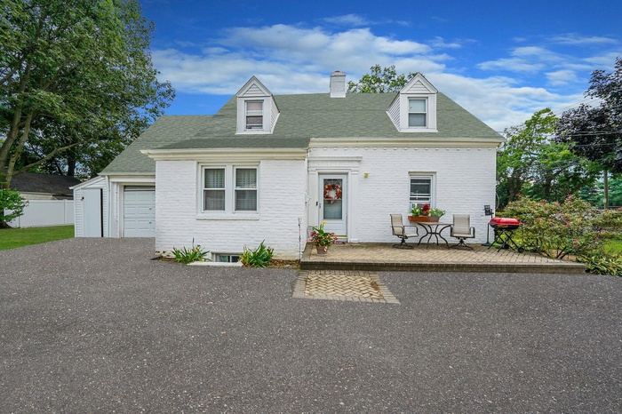 Cape cod home featuring brick siding, roof with shingles, a chimney, an attached garage, and driveway