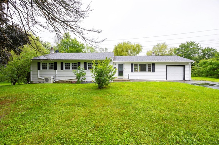 Single story home with an attached garage, a chimney, driveway, and a front lawn