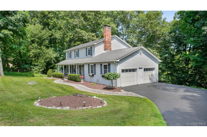 View of front facade with an attached garage, driveway, a front yard, a chimney, and covered porch