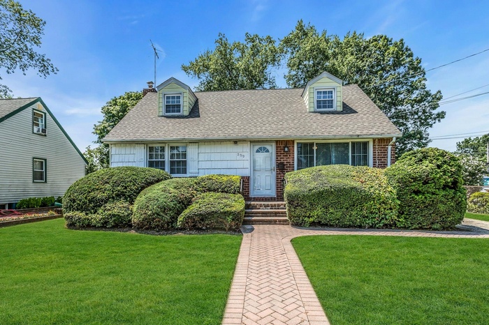 View of front of home with a shingled roof, a front yard, a chimney, and brick siding