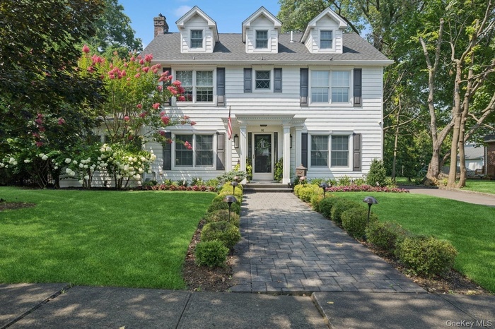 Georgian-style home with a chimney, a front yard, and roof with shingles