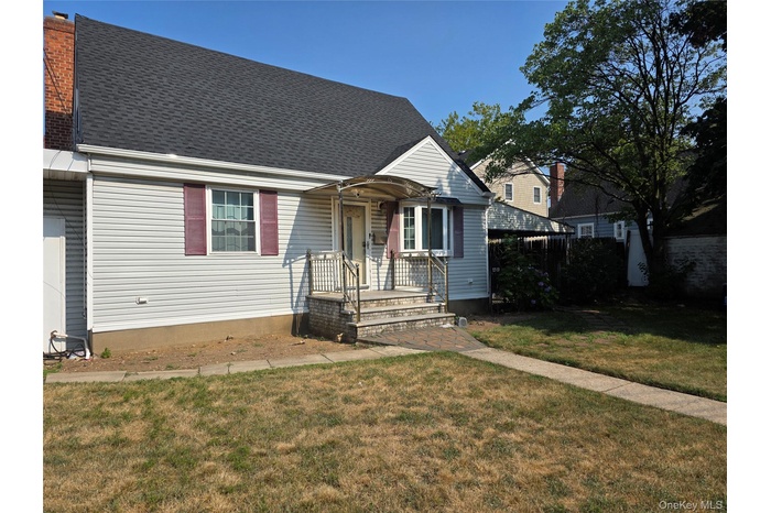 View of front facade with roof with shingles, a front lawn, and a chimney