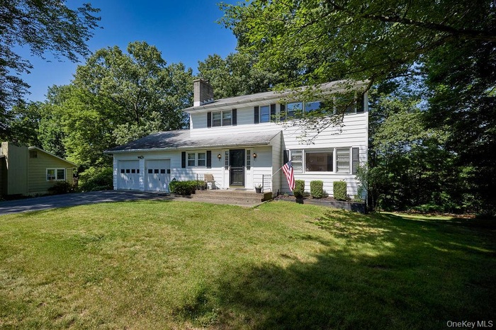 View of front of property with a garage, driveway, a chimney, and a front lawn