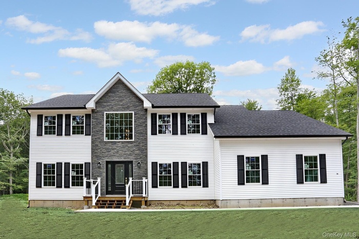 Colonial-style house with a front lawn, a shingled roof, and stone siding