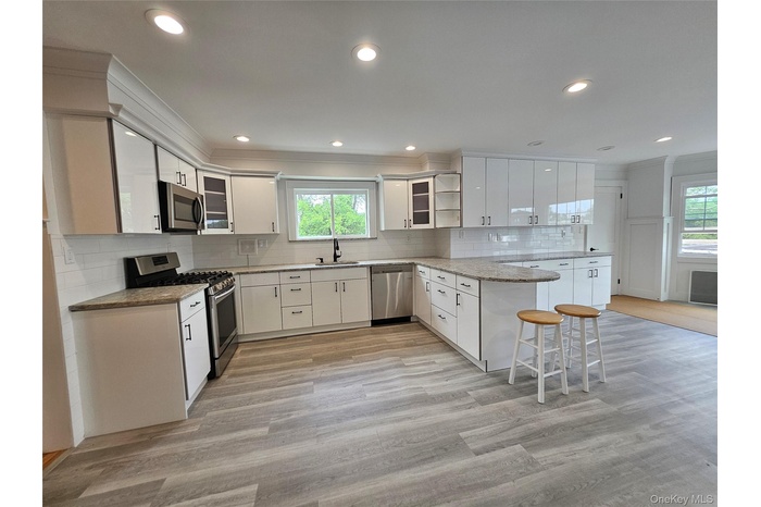 Kitchen featuring appliances with stainless steel finishes, a peninsula, ornamental molding, tasteful backsplash, and glass insert cabinets