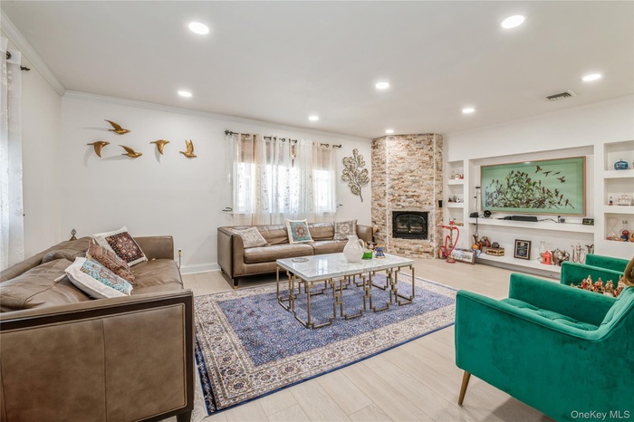 Living room with crown molding, a large fireplace, wood finished floors, recessed lighting, and built in features