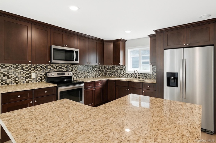 Kitchen featuring appliances with stainless steel finishes, dark brown cabinets, recessed lighting, light stone counters, and backsplash