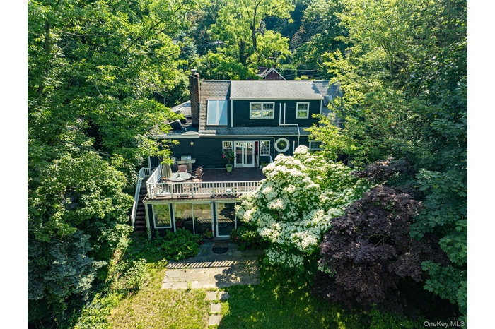 Rear view of house with a wooden deck, stairs, a chimney, and a forest view