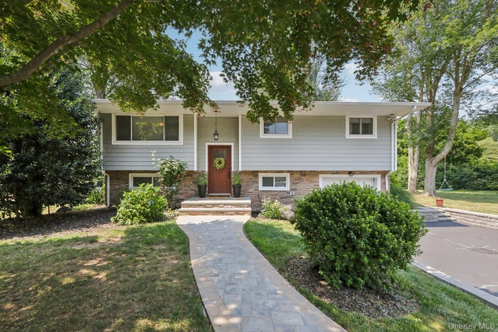 Raised ranch featuring stone siding, an attached garage, and a front lawn