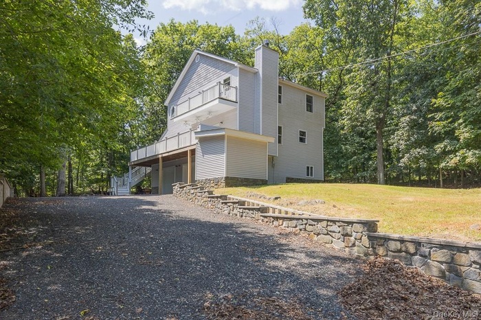 View of front of home featuring driveway, a chimney, a balcony, a front yard, and an attached garage
