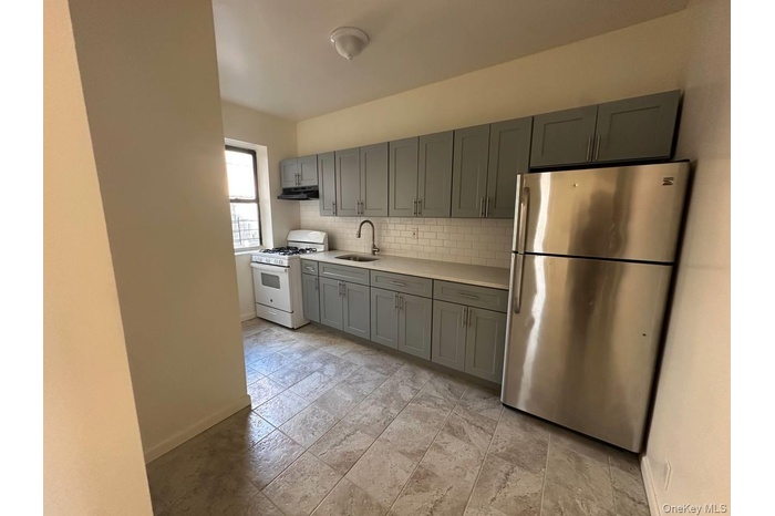 Kitchen with freestanding refrigerator, gray cabinetry, gas range gas stove, light countertops, and backsplash