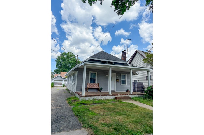 Bungalow-style house featuring covered porch, a front yard, a chimney, and a shingled roof