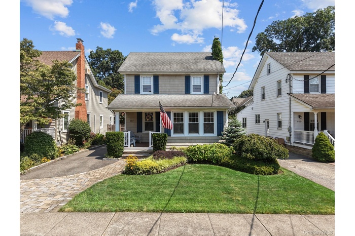 View of front of property with covered porch, a shingled roof, and a front yard