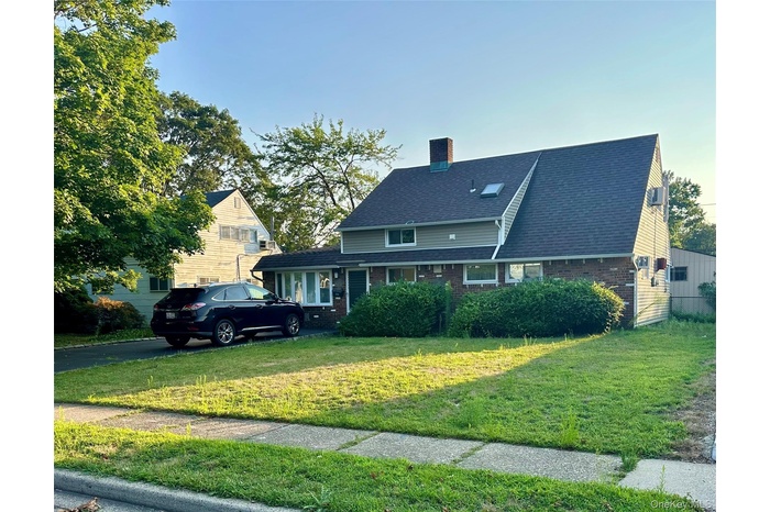 Traditional-style house featuring brick siding, a chimney, a front lawn, and a shingled roof
