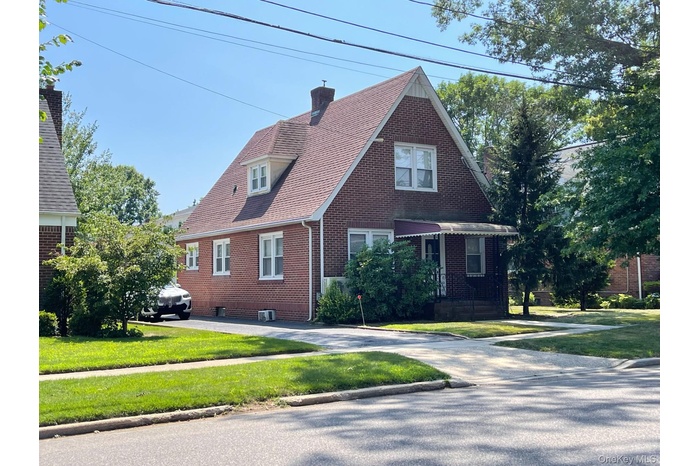 Tudor home featuring brick siding, a front lawn, a chimney, and a shingled roof