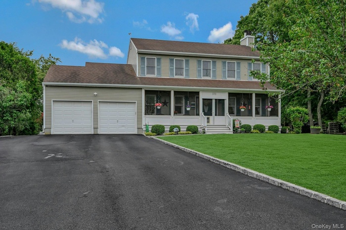 Colonial home featuring a sunroom, a garage, a front yard, asphalt driveway, and a chimney