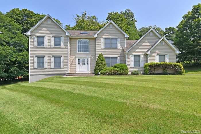 View of front of house with a front lawn and view of wooded area