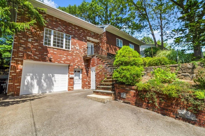 View of front of house featuring an attached garage, driveway, brick siding, and stairs