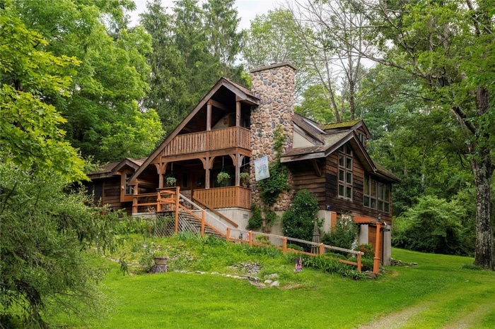 View of front facade featuring a front lawn, stairway, a balcony, a chimney, and a forest view
