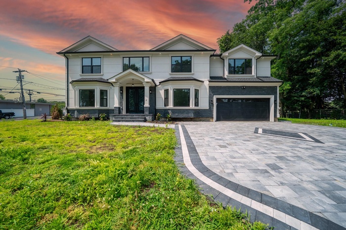 View of front of house with decorative driveway, an attached garage, a front yard, stone siding, and stucco siding