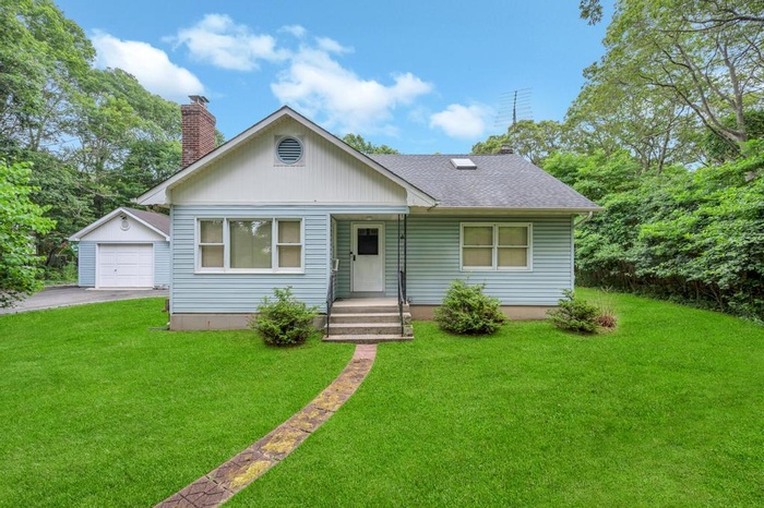 View of front of property featuring an outbuilding, driveway, a front lawn, a shingled roof, and a garage