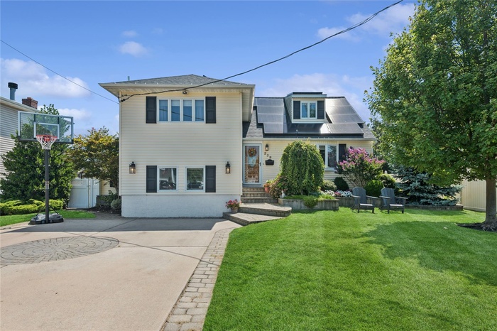 View of front of home with a front lawn, a shingled roof, driveway, and solar panels