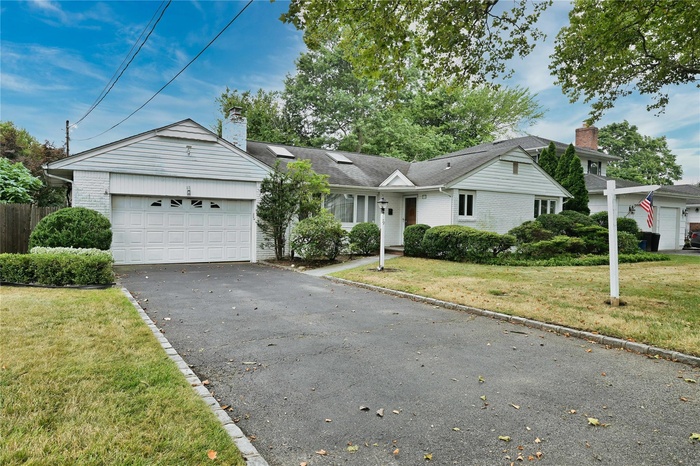 Ranch-style house featuring a garage, a front yard, driveway, brick siding, and a chimney