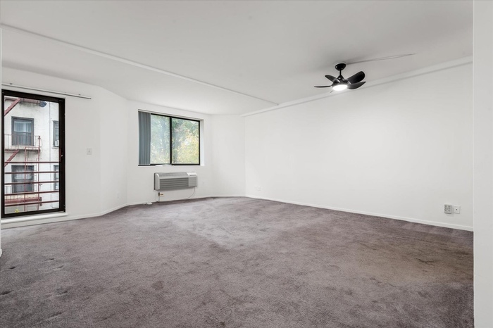Empty room featuring carpet, a wall mounted air conditioner, and ceiling fan