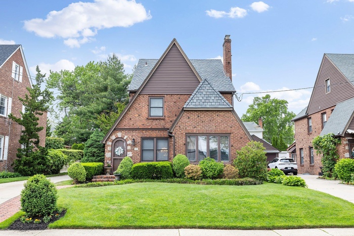 English style home with brick siding, a chimney, a front lawn, and a high end roof