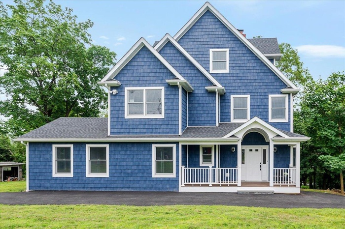 View of front of property with covered porch, a front lawn, roof with shingles, and a chimney