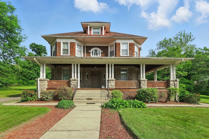 American foursquare style home featuring covered porch, stone siding, and a front lawn