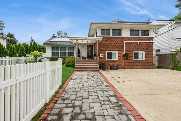 View of front of property featuring brick siding, solar panels, and a patio area