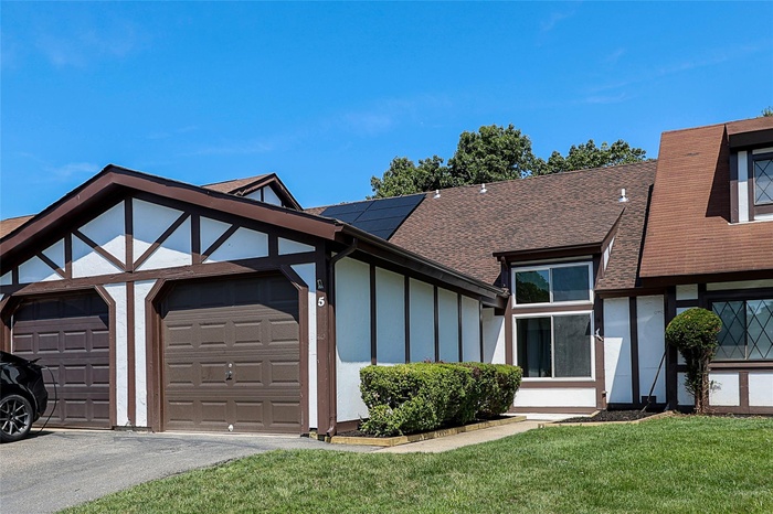 Tudor house with a shingled roof, a front yard, a garage, solar panels, and asphalt driveway