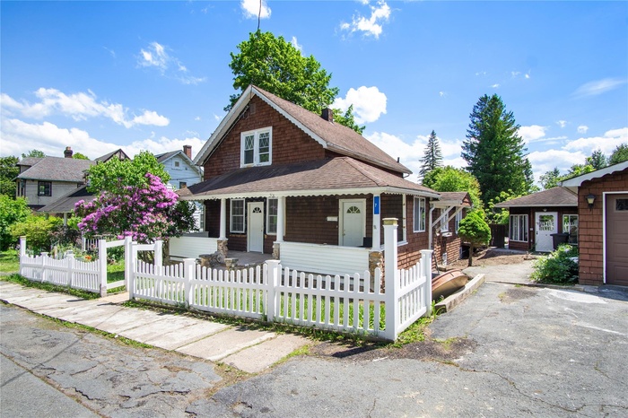 View of front of home with covered porch, a fenced front yard, and a shingled roof