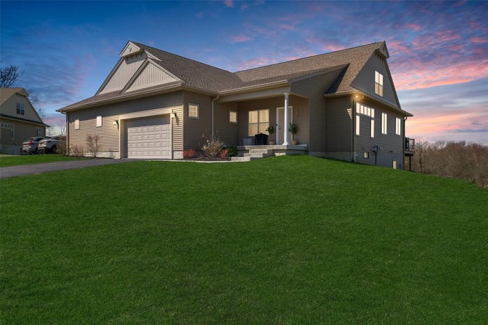 View of front facade featuring an attached garage, covered porch, aphalt driveway, and a front yard