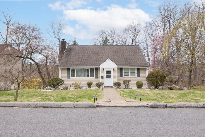 Cape cod-style house featuring a chimney, a front lawn, and a shingled roof