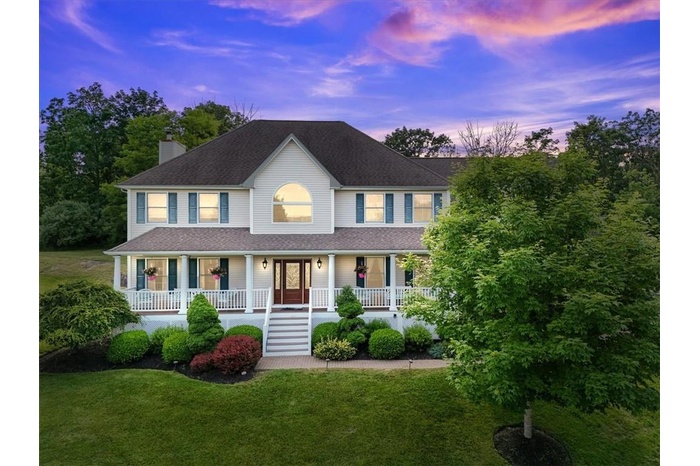 Colonial house featuring a porch and a beautifully landscaped lawn