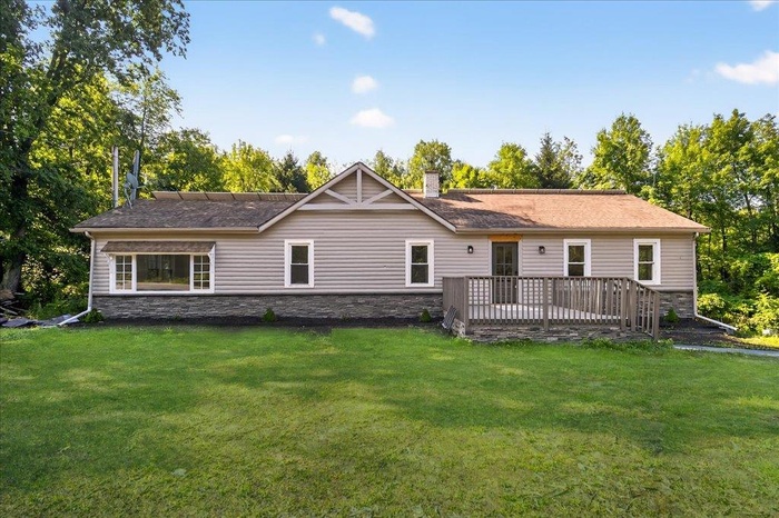 Rear view of house featuring stone siding, a chimney, a yard, and a wooden deck