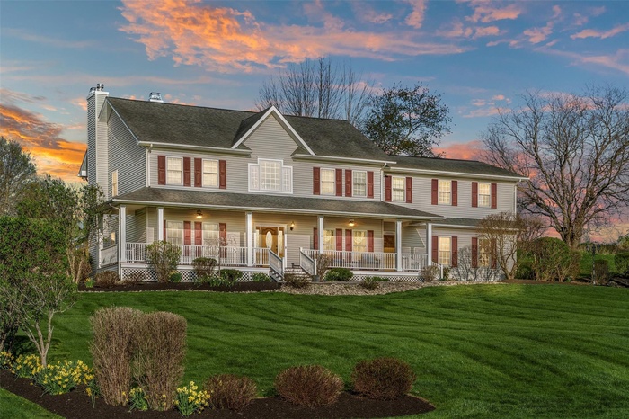 Back of house at dusk with a chimney, covered porch, and a yard