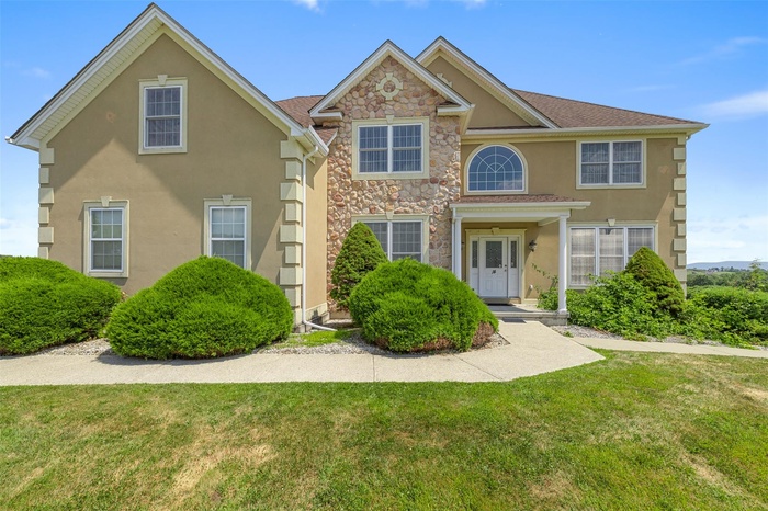 View of front of property with stucco siding, a front lawn, and stone siding