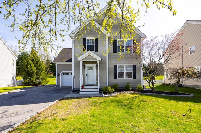 Traditional-style house featuring an attached garage, asphalt driveway, and a front yard