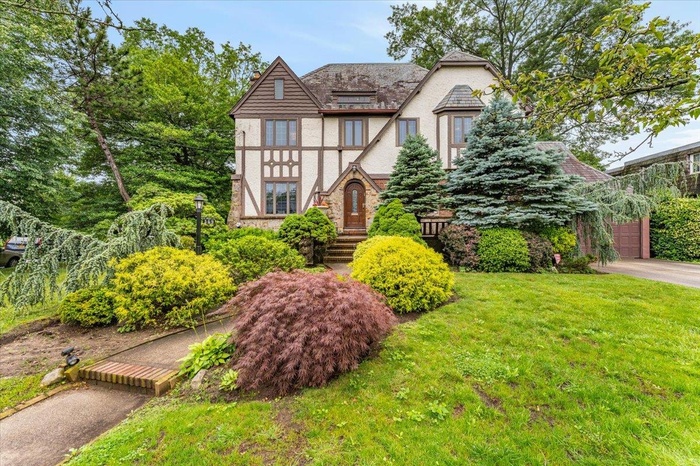 English style home featuring stucco siding, a front yard, a garage, stone siding, and driveway